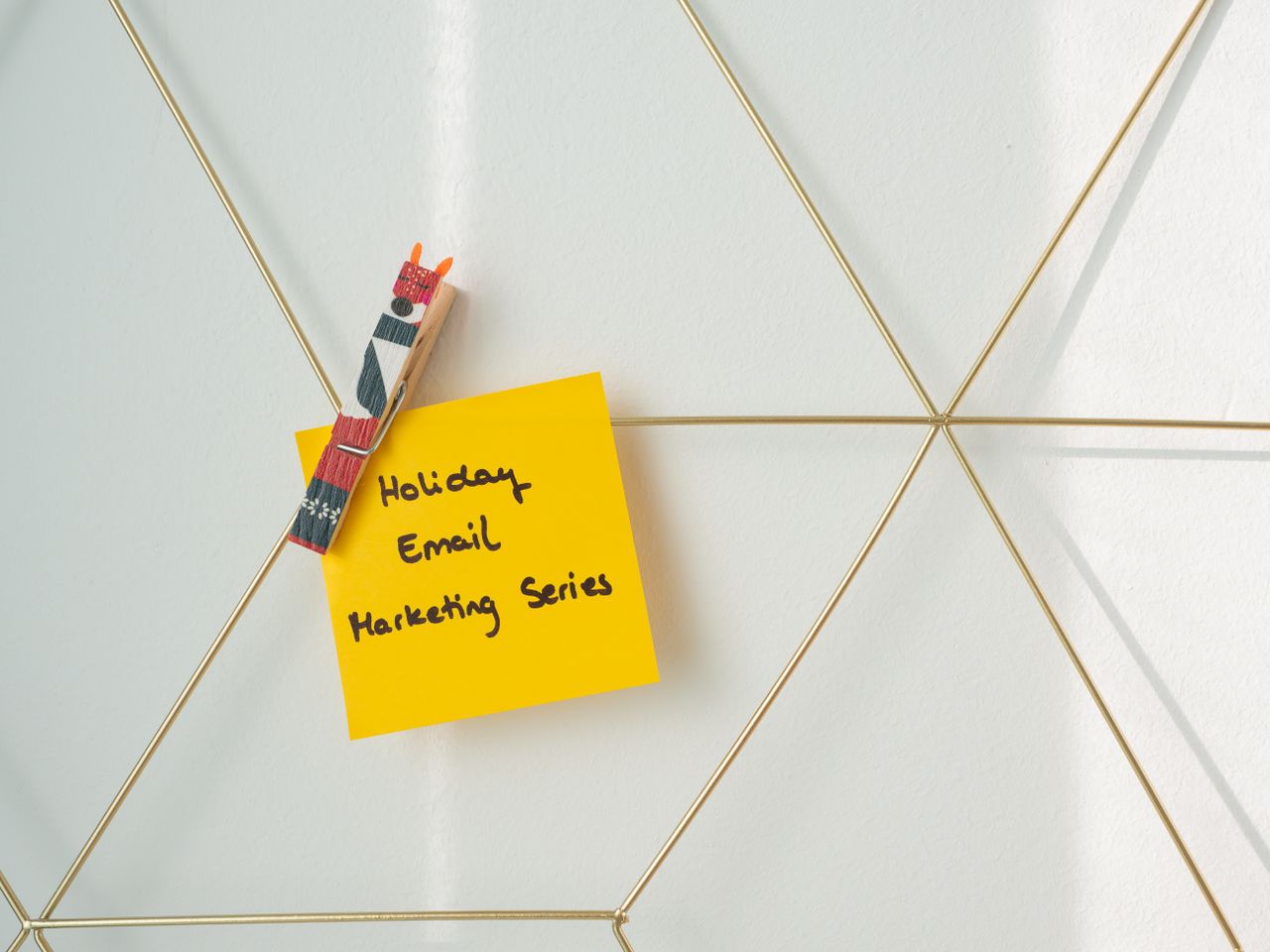 Post-it jaune vif avec un message de marketing par email pour les fêtes, fixé sur un mur de wireframe.